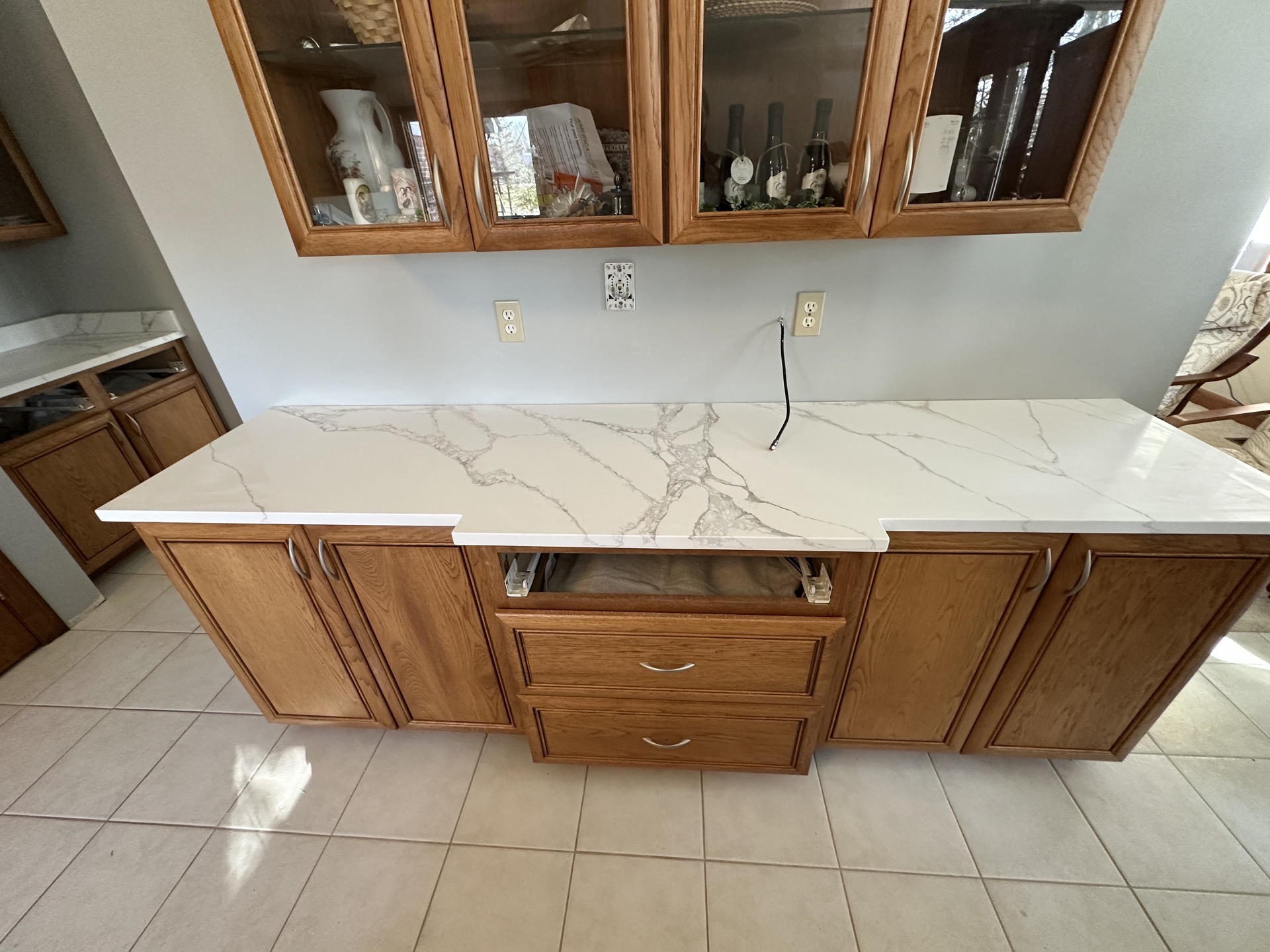 Long white stone countertop with soft grey veining installed on existing oak cabinetry in a bright kitchen