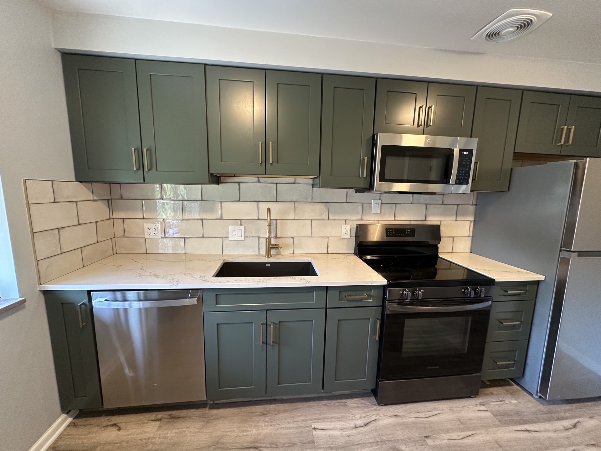 Kitchen with deep green cabinets, white stone countertops, gold faucet, and a handmade subway tile backsplash
